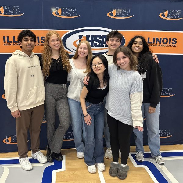 Sophomore Anshul Nadendla, senior Anna Gustafson, junior Sarah Fitzgerald, seniors Emily Won, Danny Pashkow, Kyra Sarantapolous and Neha Doppalapudi (from left to right) pose in front of an IHSA banner at the Heartland Community College gym. They began competing at 9:30 a.m. and ended at 1:00 p.m. Photo by Laura Minerva.